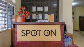 A reception desk with a "SPOT ON" sign, framed certificates on the wall, and a potted plant with red flowers. - Spot On 1847 Hotel Maya (Beru)