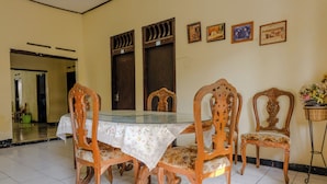 A dining area with a glass-top table, wooden chairs with floral upholstery, and a tiled floor. - Spot On 1847 Hotel Maya (Beru)