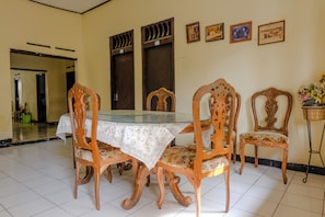 A dining area with a glass-top table, wooden chairs with floral upholstery, and a tiled floor. - Spot On 1847 Hotel Maya (Beru)