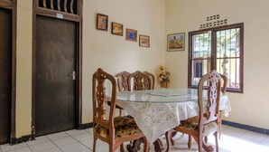 A dining area with a glass table, wooden chairs, a closed door, and wall-mounted pictures. - Spot On 1847 Hotel Maya (Beru)