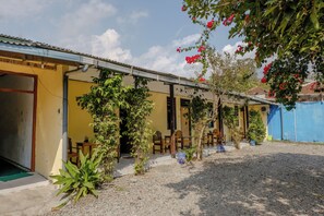 A building with a yellow facade, outdoor seating area, and a gravel ground. - Spot On 1847 Hotel Maya (Beru)