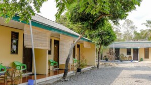 A building with a yellow exterior, green chairs outside, and a gravel courtyard. - Spot On 1847 Hotel Maya (Beru)