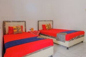 Two beds with red and blue bedding, pillows with geometric patterns, and a small table with a bottle and a box. - Spot On 1847 Hotel Maya (Beru)
