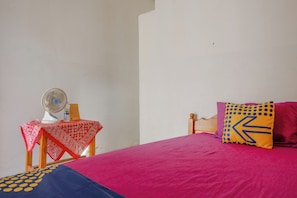 A bed with a red bedspread, a wooden headboard, and a pillow with a yellow and blue design.