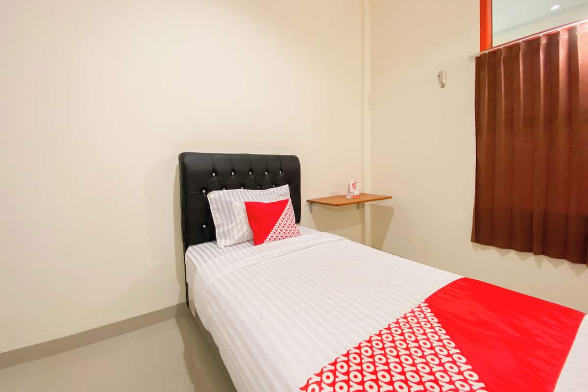 A neatly made bed with a striped white and red bedspread, a black upholstered headboard, and a small bedside table with a red object on it.