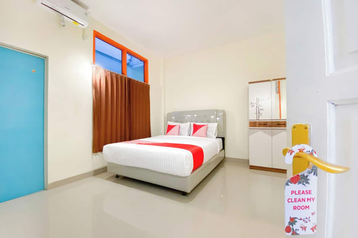 A hotel room with a bed, a blue door, a window with curtains, a bedside table, and a mirror.