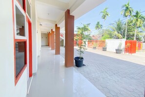 Un pasillo con suelo de baldosas, ventanas de marco rojo y una planta en maceta.