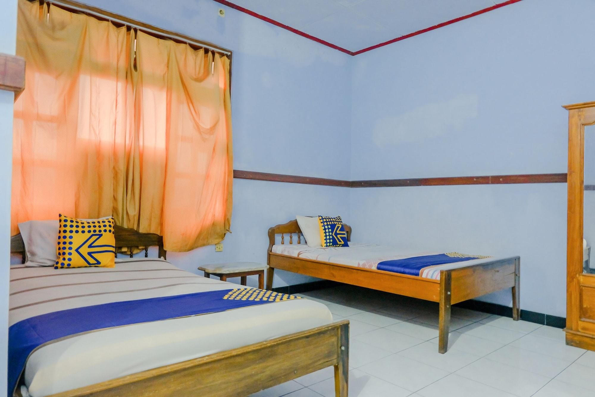 A bedroom with two beds, a wooden wardrobe, and a window with curtains.
