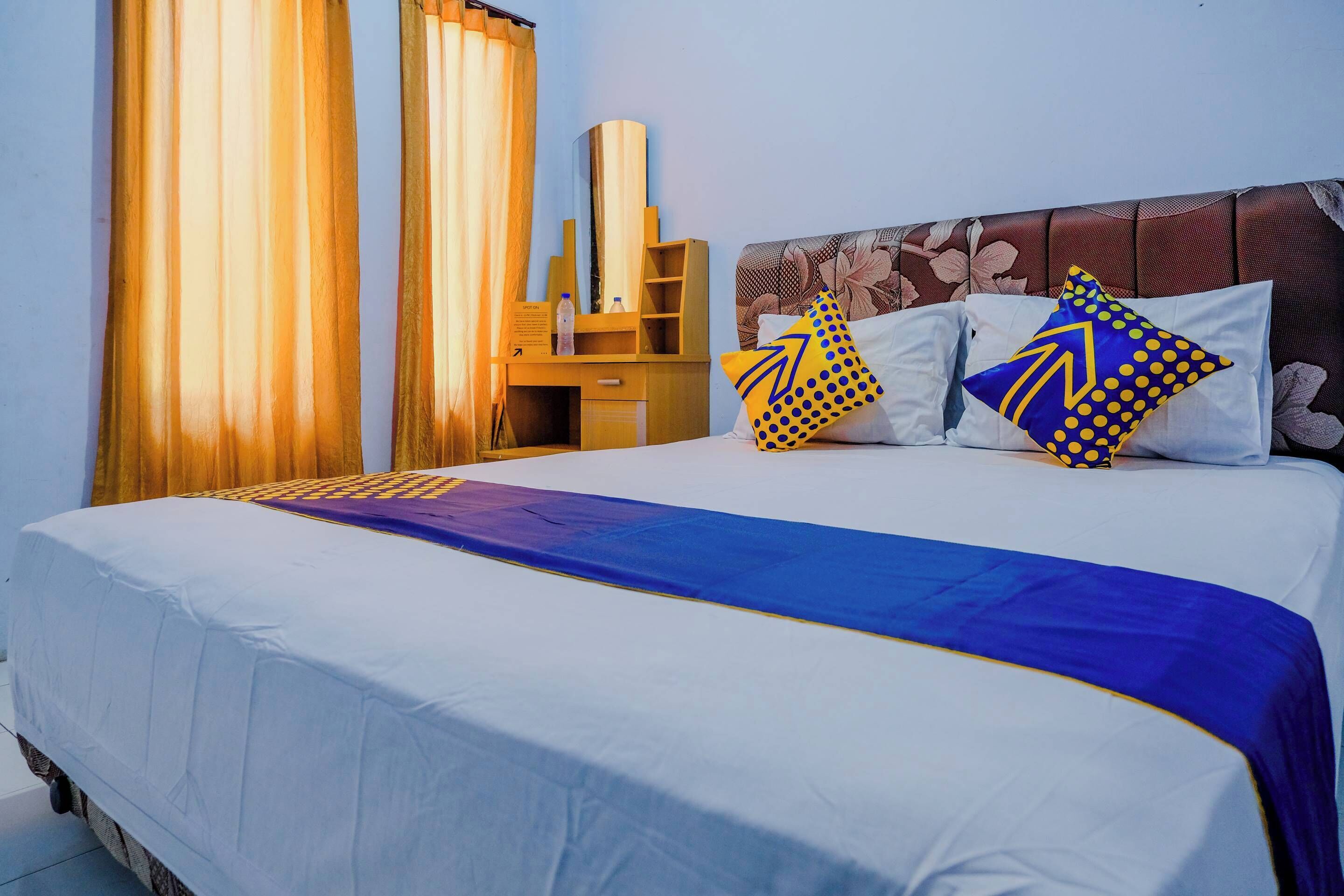 Ein Hotelzimmer mit Bett, Vorhängen, einem Holztisch und einem Spiegel.