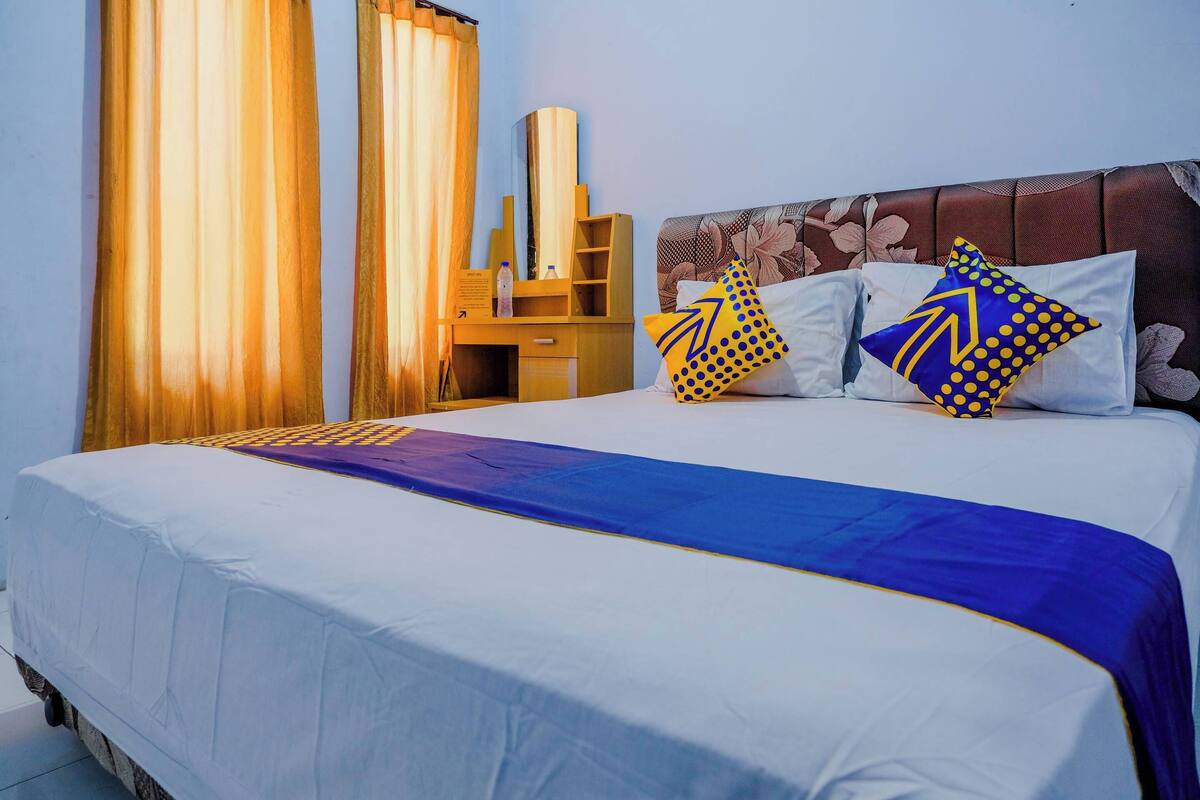 A hotel room with a bed, curtains, a wooden desk, and a mirror.