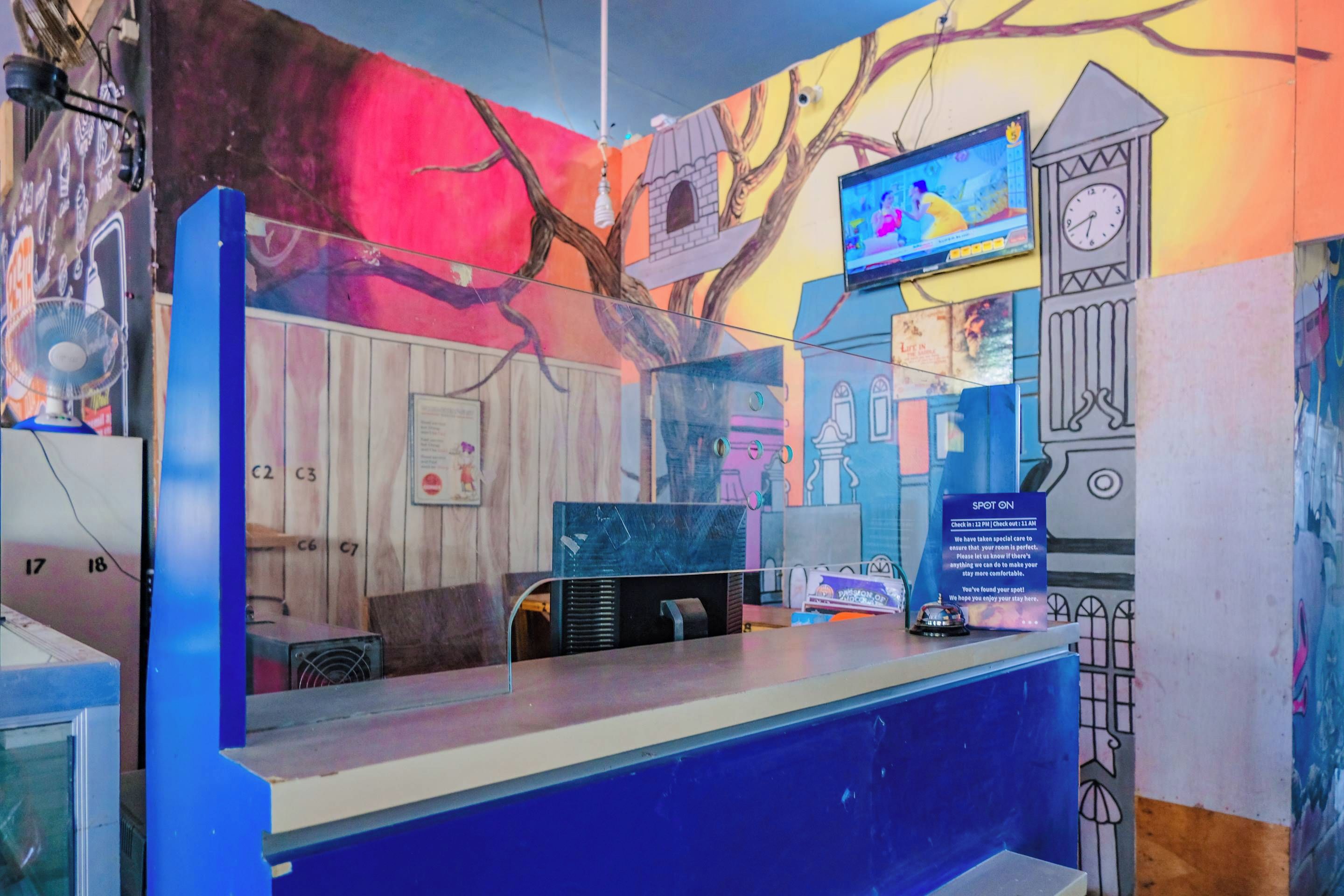 A reception desk with a blue counter, a clock, a television, and a wall with a mural.