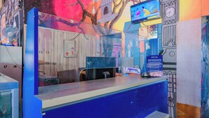 A reception desk with a blue counter, a clock, a television, and a wall with a mural. - Spot On 1958 Asembagus Family (Asembagus)