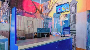 Un mostrador de recepción con una barra azul, un reloj, un televisor y una pared con un mural.