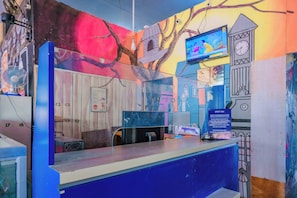 A reception desk with a blue counter, a clock, a television, and a wall with a mural. - Spot On 1958 Asembagus Family (Asembagus)