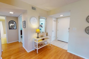 A hallway with a white console table, a lamp, and a mirror. There are doors on both sides, and a window with a decorative frame. - Across from Beach, Stunning Canal Views, Age 55 up (Siesta Key)