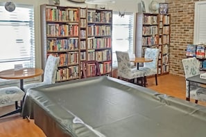 Une pièce avec une grande bibliothèque, une table de billard et deux fauteuils.