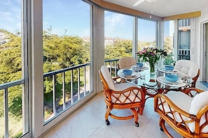 Un balcon avec une table et des chaises, de grandes fenêtres et une vue sur la verdure.