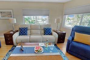 A living room with a beige sofa, a blue armchair, and a coffee table with a watermelon slice and glasses.