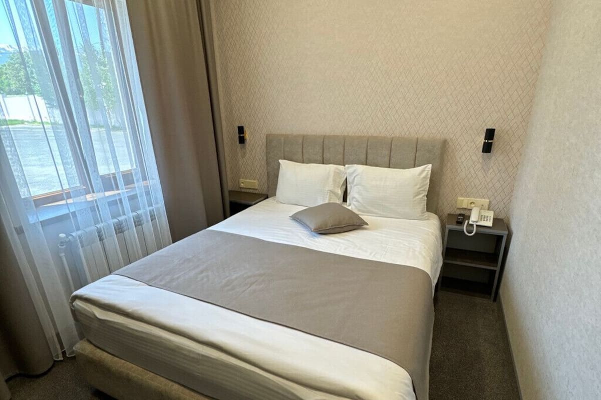 A hotel room with a large bed, a nightstand, a telephone, and a window with curtains.