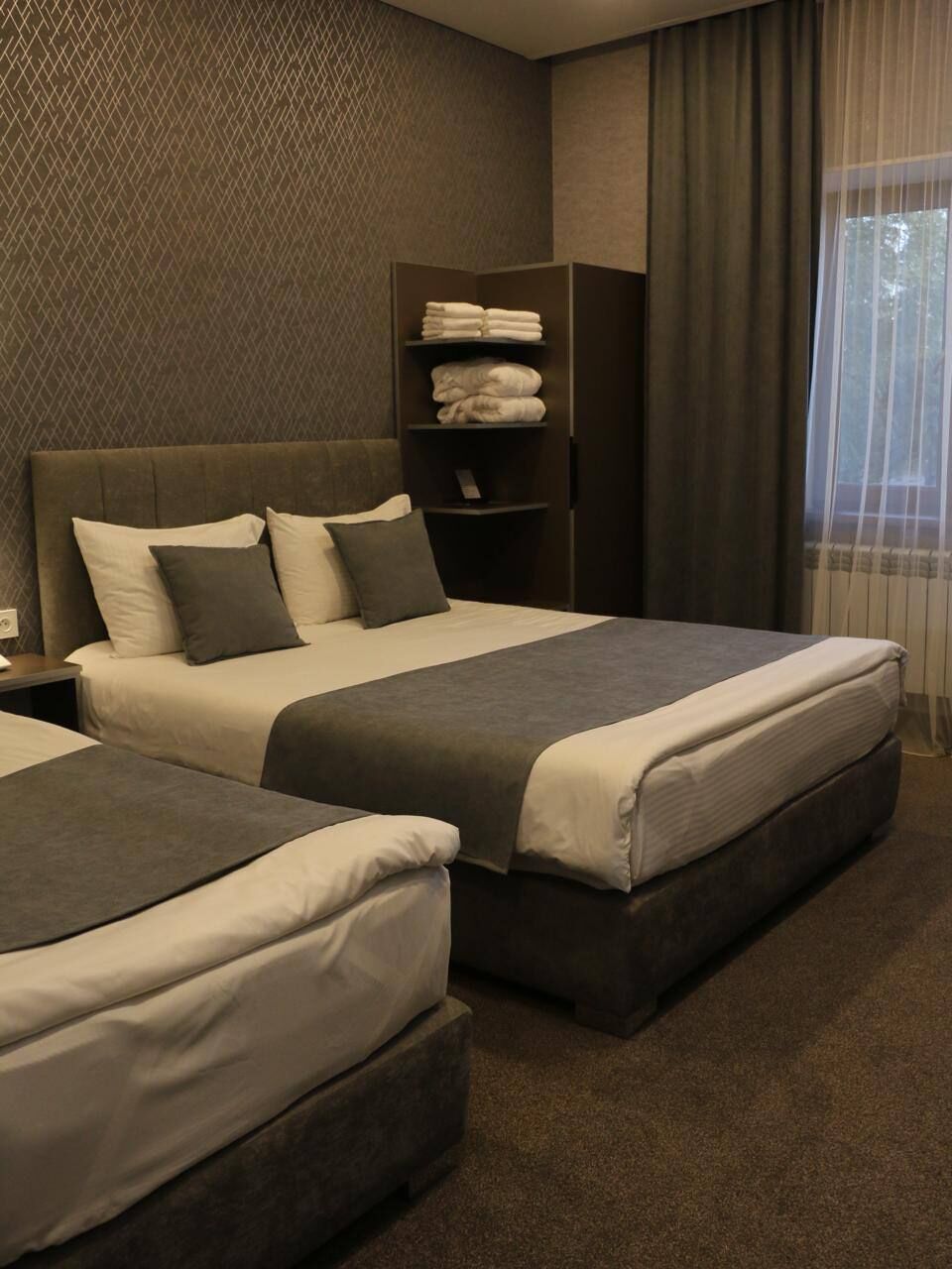 Una habitación de hotel con dos camas, un cabecero oscuro, una mesita de noche y un armario.