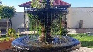 Una fuente de varios niveles con agua cayendo, sobre un cielo azul despejado.