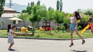 Un parque infantil con toboganes y columpios, una cancha de tenis y un edificio al fondo.
