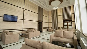 Un vestíbulo moderno con sofás color beige, un televisor de pantalla plana y un suelo con diseño de mármol.