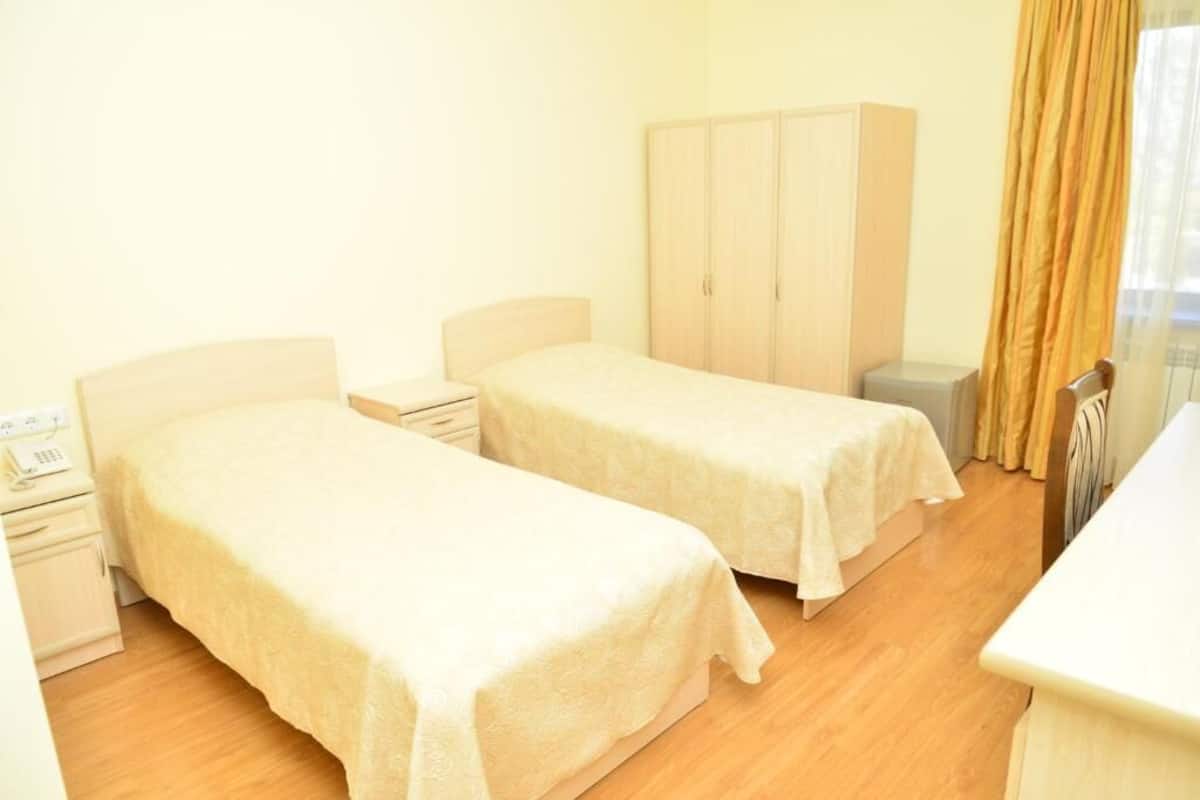 A room with two single beds, a wardrobe, a bedside table with a lamp, and a small desk with a telephone.