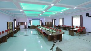Una sala de conferencias con una larga mesa, sillas rojas y una pantalla para proyector.