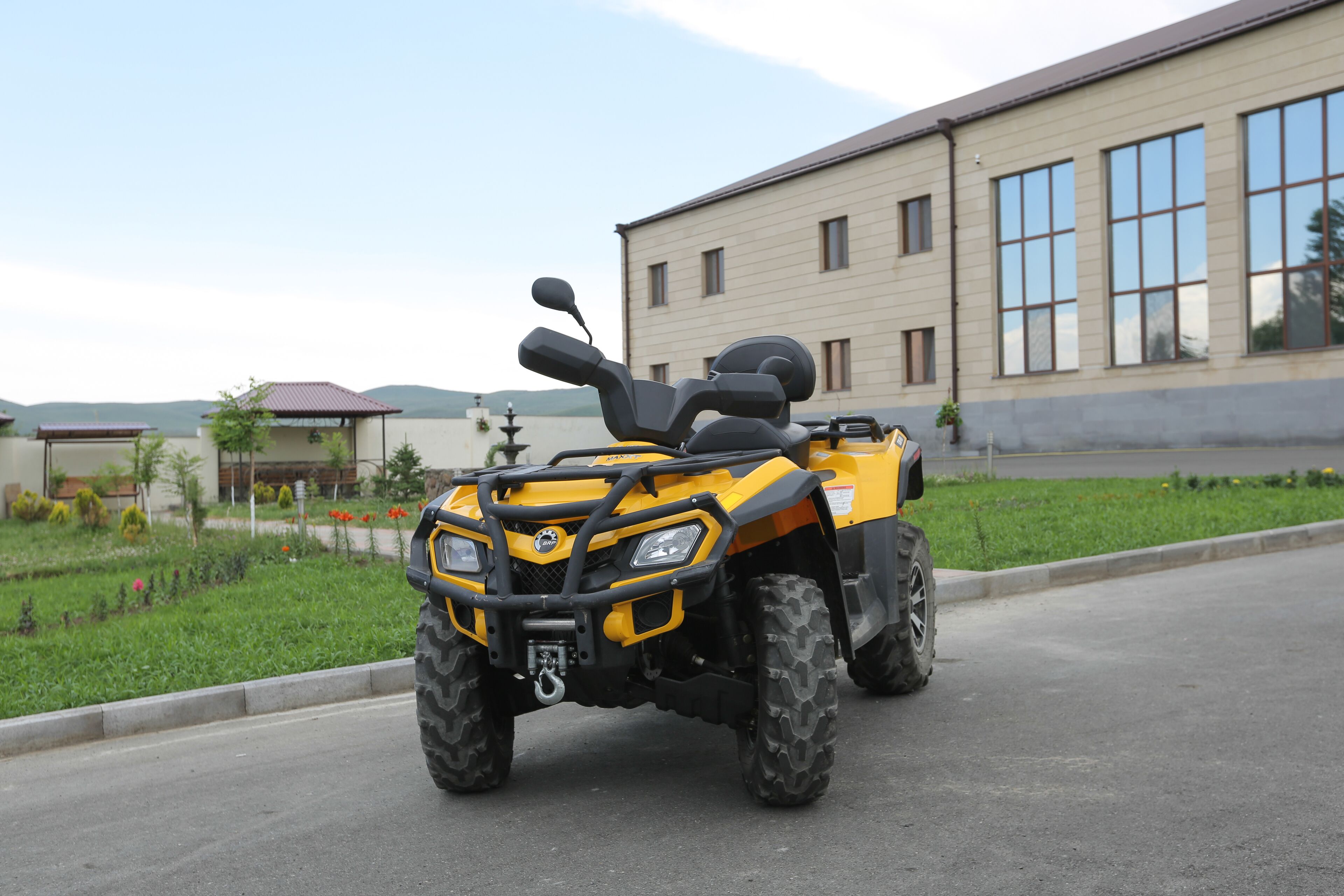 Un veicolo fuoristrada giallo parcheggiato di fronte a un edificio con ampie vetrate e un'area pavimentata con vegetazione.