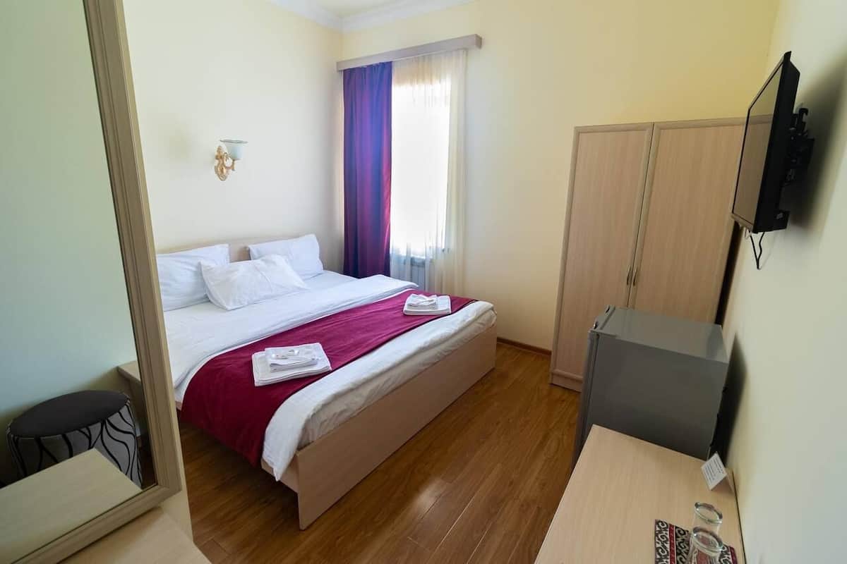 A hotel room with a bed, a television, a wardrobe, and a small table with a glass.