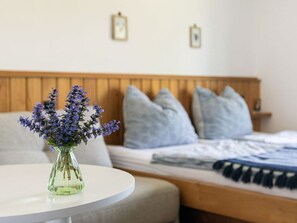 A bed with a wooden headboard, a round white table with a vase of flowers, and two framed pictures on the wall.