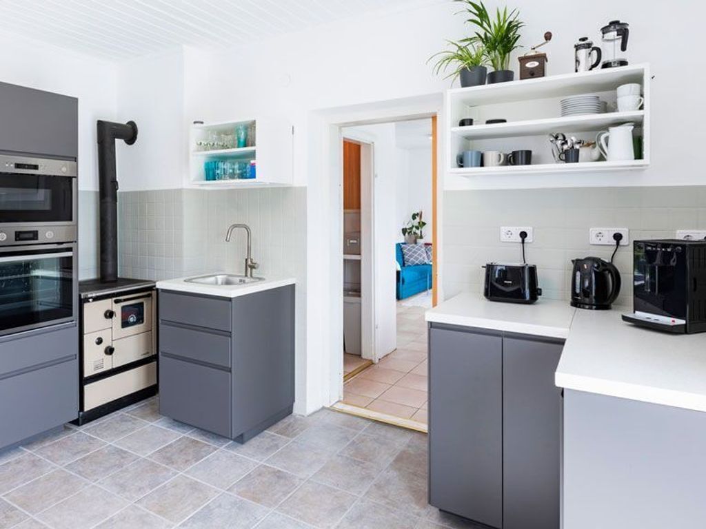 Une cuisine moderne avec des meubles gris, un four encastré, un évier et une machine à café.