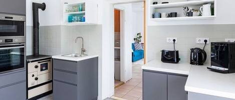 A modern kitchen with grey cabinets, a built-in oven, a sink, and a coffee machine.