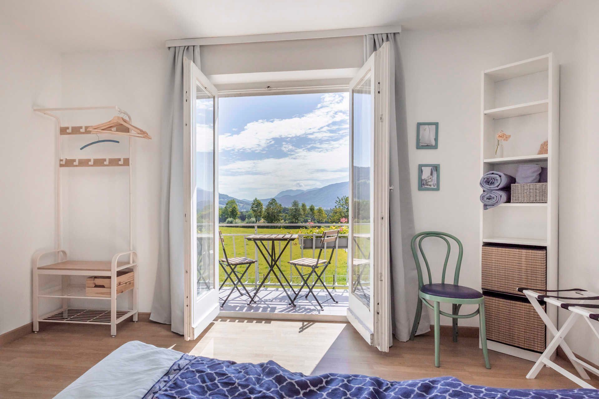 Ein Zimmer mit Bett, Stuhl, Tisch, einem Balkon mit Bergblick und einem Kleiderschrank.