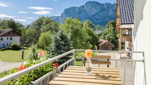 Un balcón con una mesa de madera, un florero con una flor y vistas a la montaña.