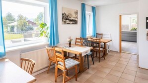 Ein Essbereich mit Tisch und Stühlen, einem Heizkörper, einem Fenster mit Vorhängen und einem Bild an der Wand.