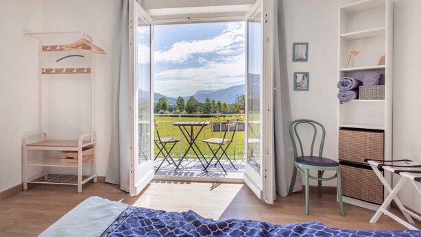 Una habitación con cama, silla, mesa, balcón con vistas a las montañas y armario.