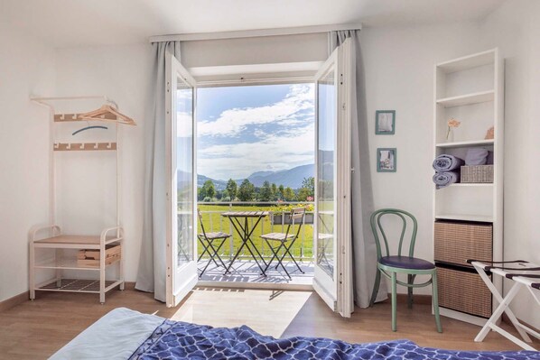 Una habitación con cama, silla, mesa, balcón con vistas a las montañas y armario.