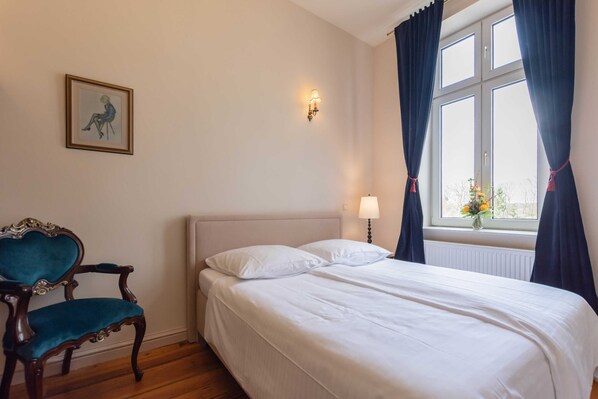 A bedroom with a bed, a chair, a wall-mounted light, and a window with curtains.