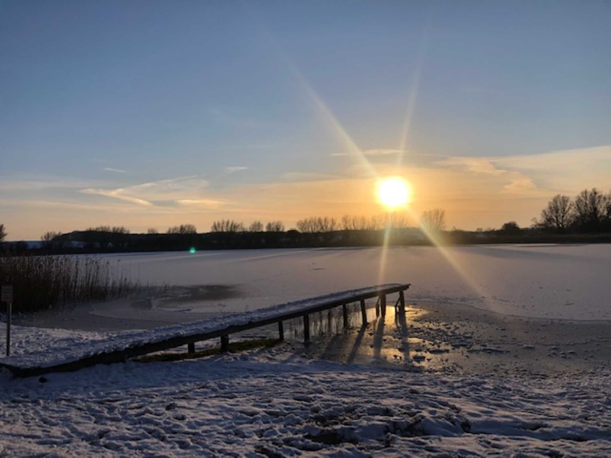 A bench in a snowy outdoor area with a sunset in the background.