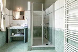 Une salle de bain avec une douche à parois de verre, un lavabo avec un miroir au-dessus et un porte-serviettes.