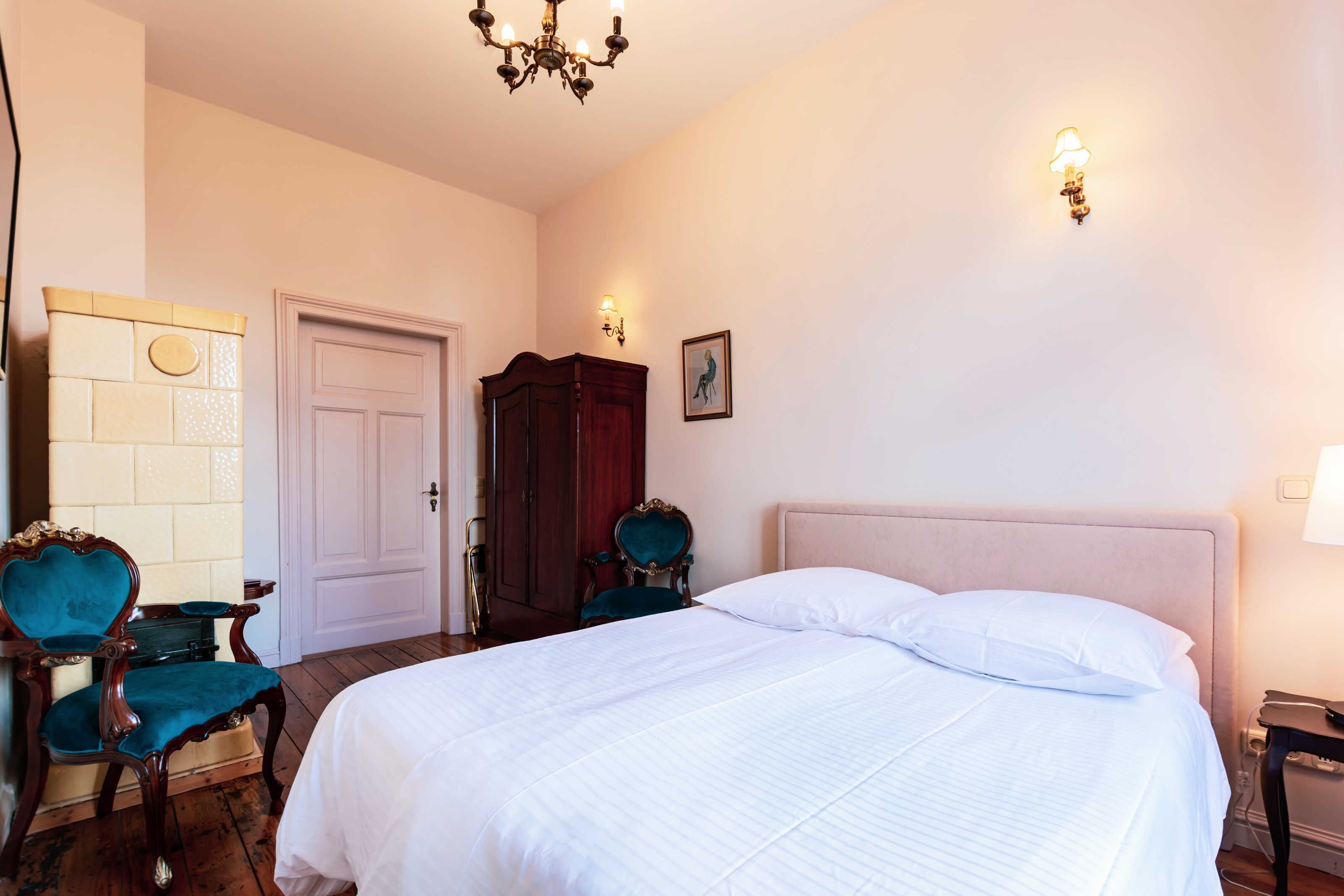 Une chambre à coucher avec un grand lit, une armoire en bois, une chaise et un lustre.