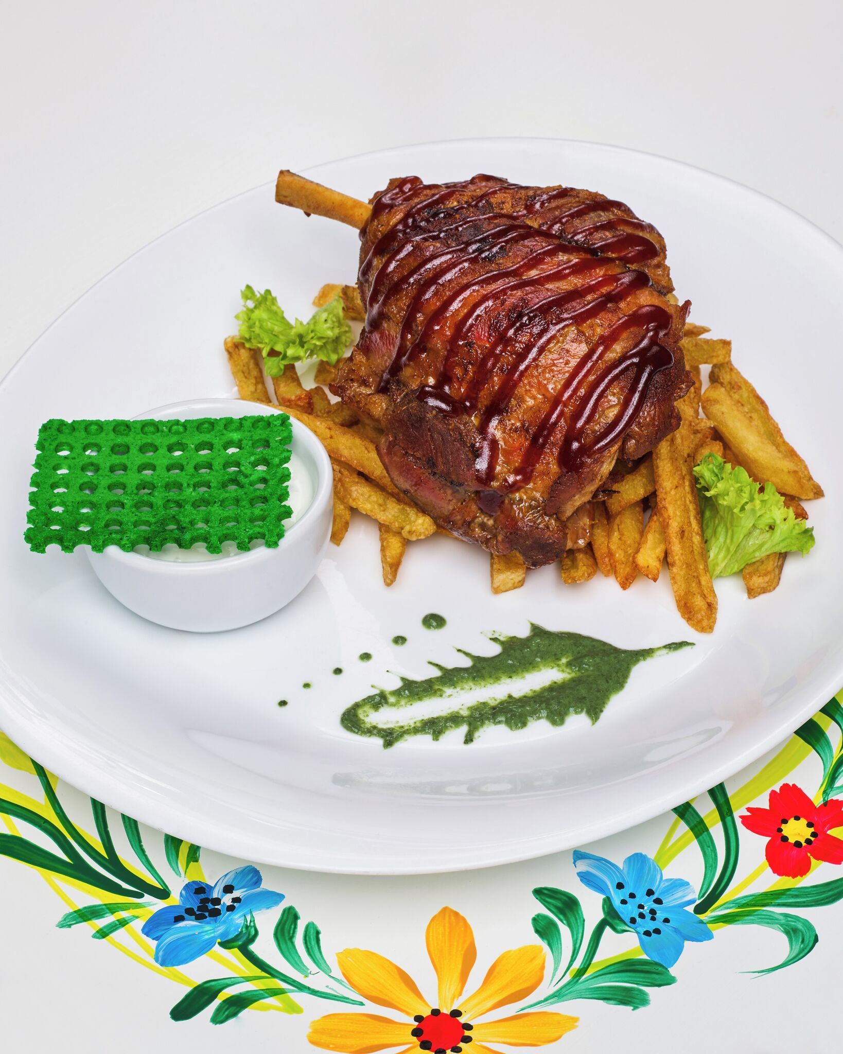 A plate with a roasted leg of lamb, fries, and a small bowl of sauce.