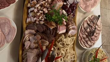 A variety of meats and cheeses arranged on a wooden board, with tongs and a sprig of parsley for decoration.