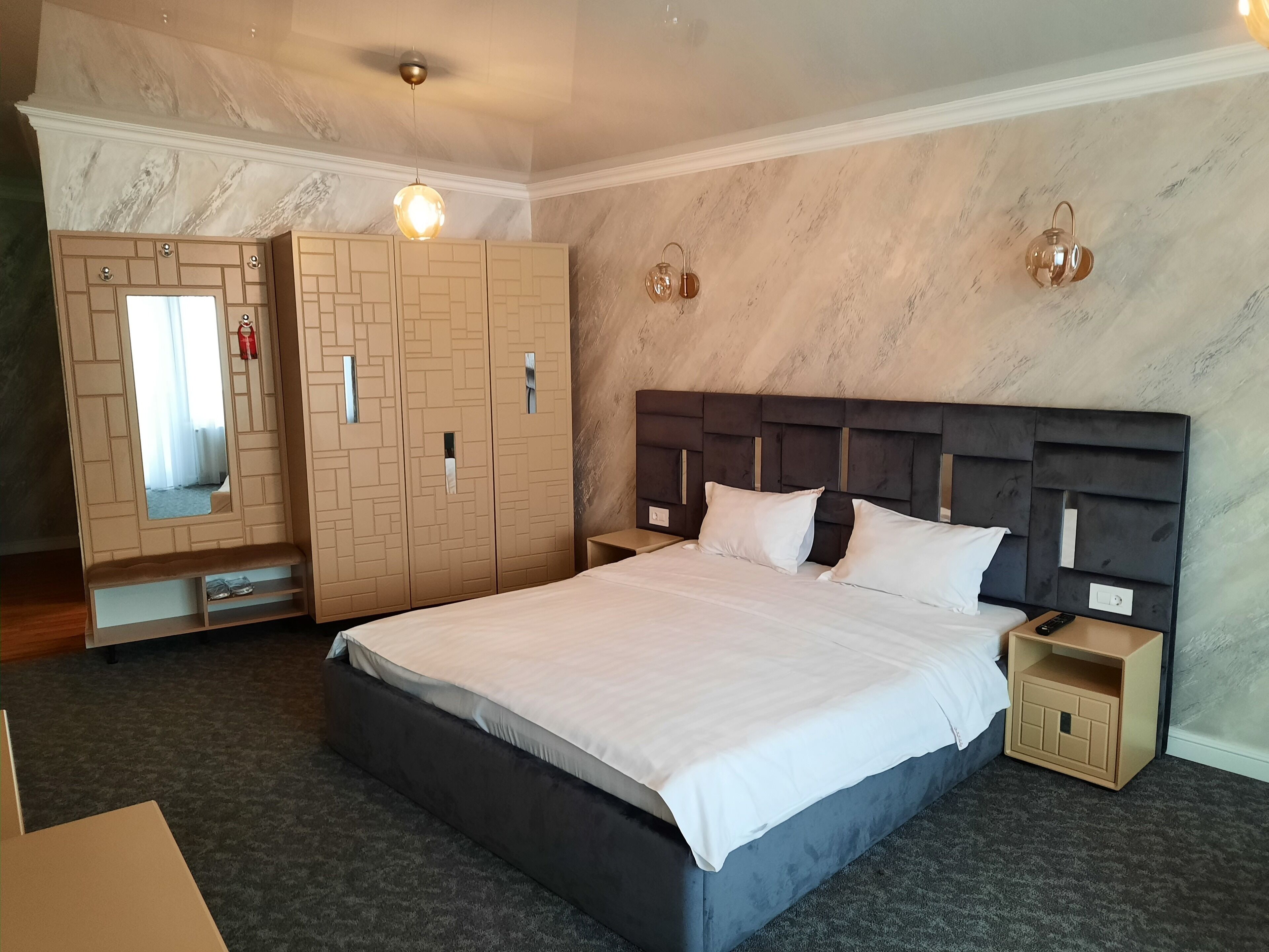 Habitación de hotel con una cama grande, un armario con puertas de espejo, una mesita de noche y un buró.