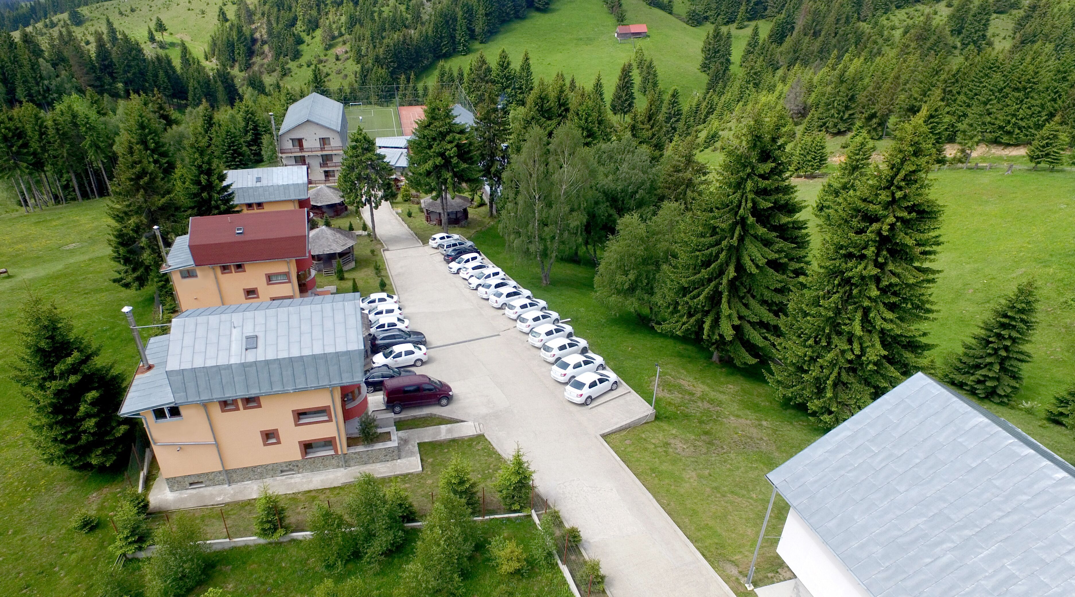 Vista aérea de una zona residencial con varios edificios, un estacionamiento y colinas boscosas circundantes.