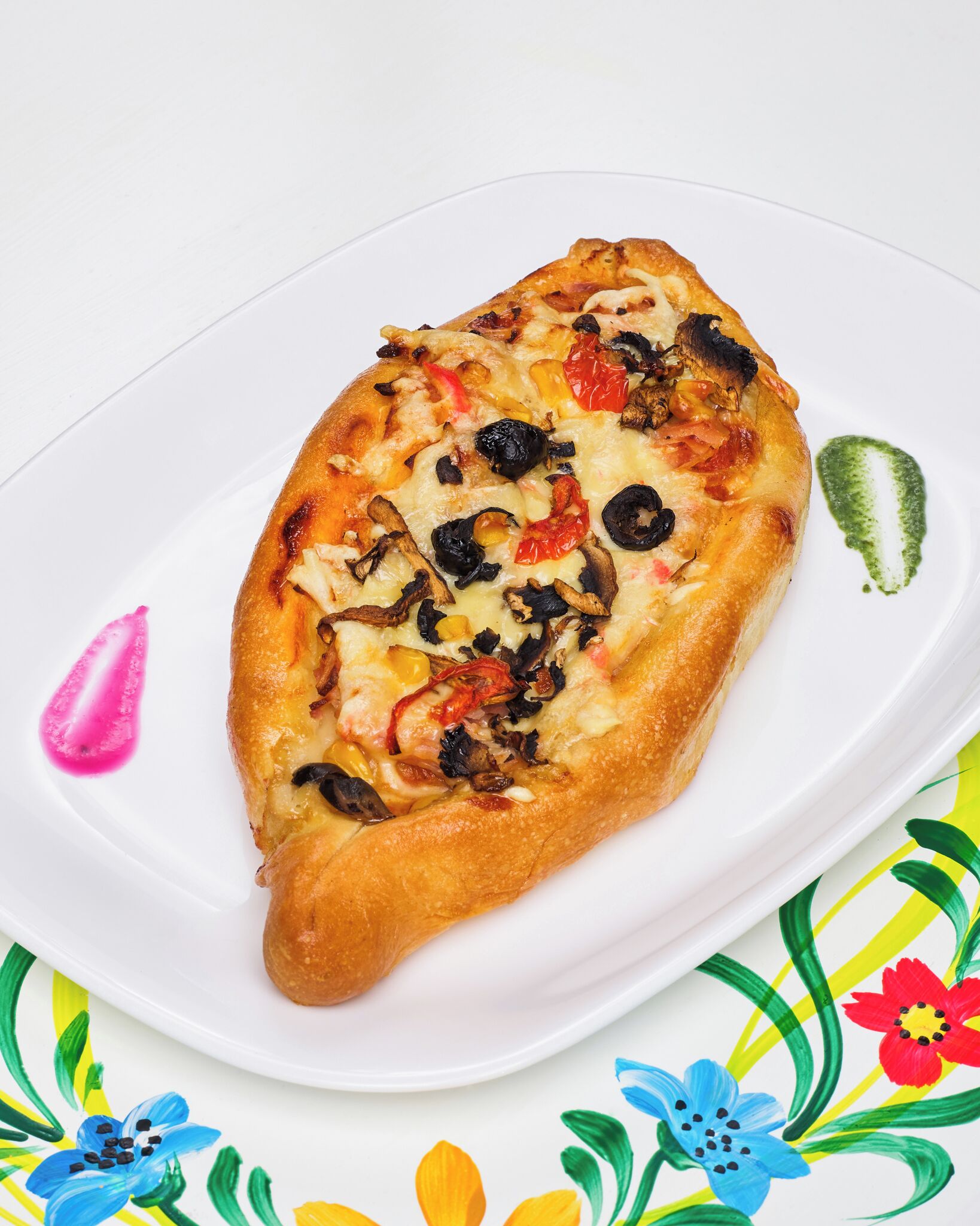 A pizza on a white plate with a floral tablecloth.
