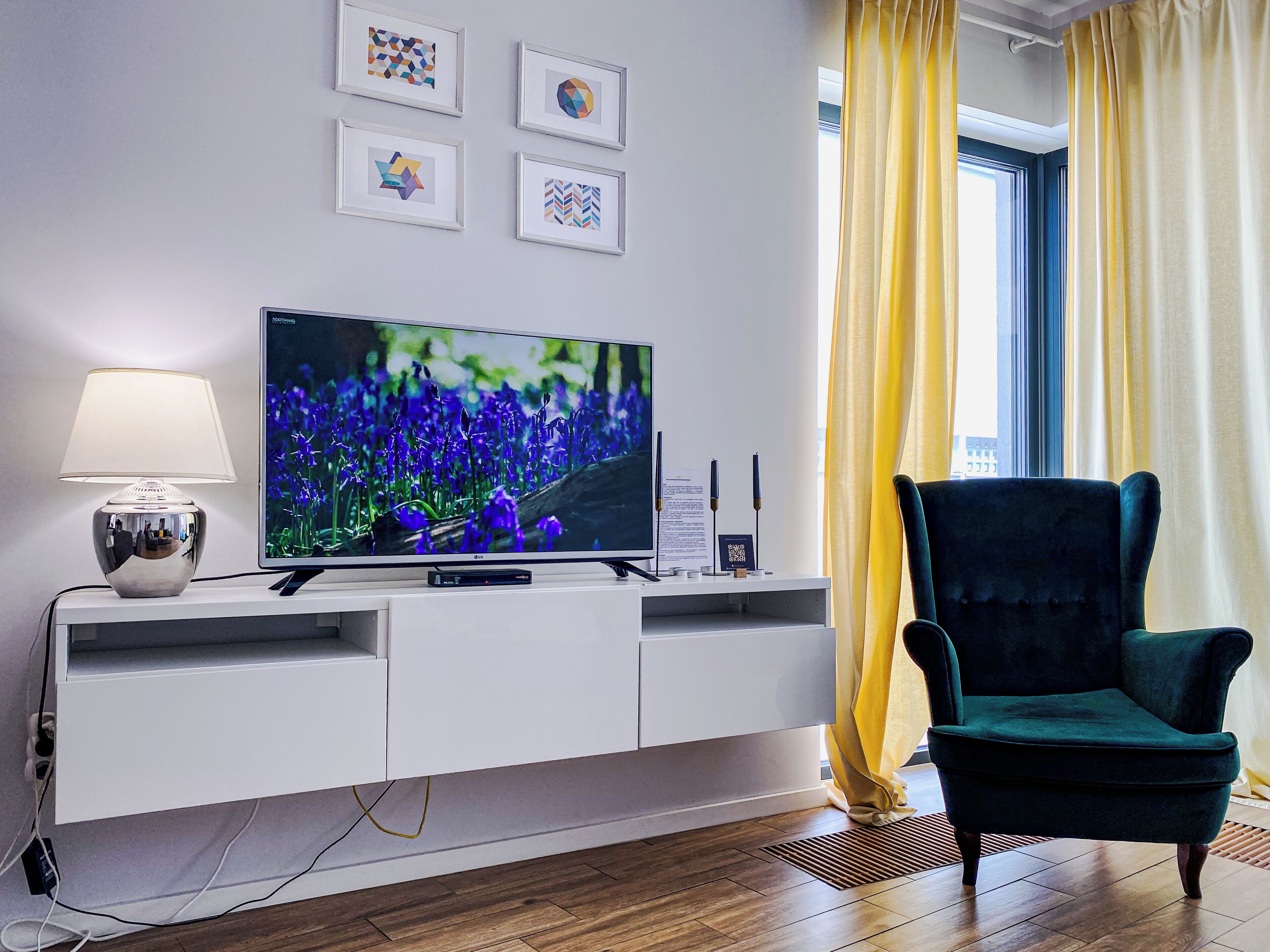 Un salon moderne avec un téléviseur à écran plat, un meuble de rangement blanc, un fauteuil vert et une fenêtre agrémentée de rideaux jaunes.