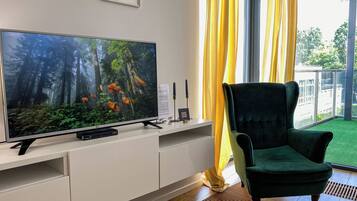 Un salon avec un téléviseur à écran plat, un fauteuil vert foncé et une fenêtre ornée de rideaux jaunes.